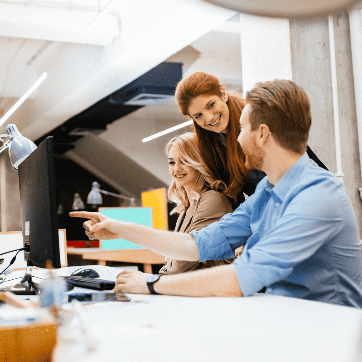 Group of people happily having a work chat, a man points his finger to a computer screen